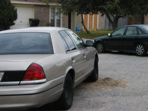 1999 Ford Crown Victoria - A tan sedan is parked on a gravel driveway next to a house, with another car behind it.