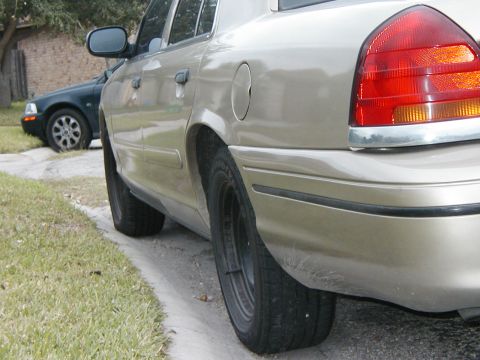 1999 Ford Crown Victoria - Rear view of a tan sedan parked on a residential street, with another dark sedan visible in the background.