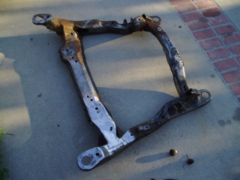 1993 Ford Taurus - A rusty subframe part lies on a concrete surface.