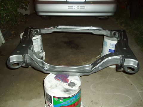 1993 Ford Taurus - A subframe part is shown resting on buckets, with the rear of a car displaying a SHO badge visible in the background.