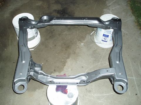 1993 Ford Taurus - Automotive subframe painted gray and supported by buckets on a concrete surface.