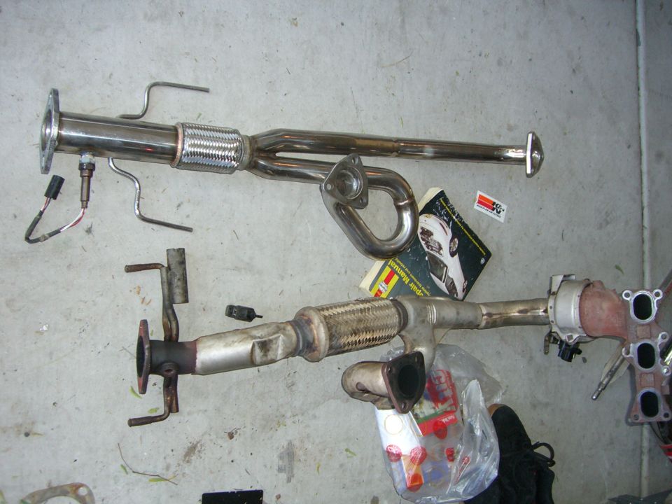 Two exhaust systems laid out on concrete, one shiny and one with a catalytic converter