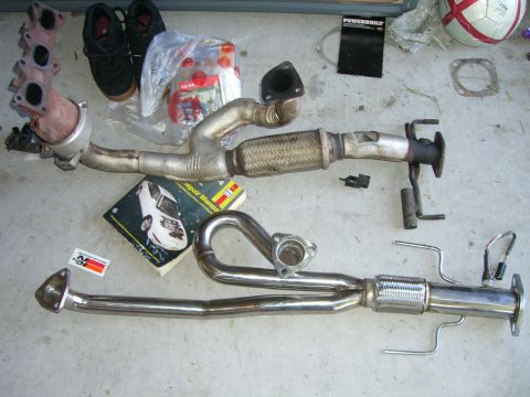 1996 Ford Probe - Various exhaust system components are displayed on a concrete surface, alongside a repair manual and a pair of shoes.