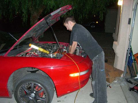 1996 Ford Probe - A person is working on the engine of a red car in a driveway at night.