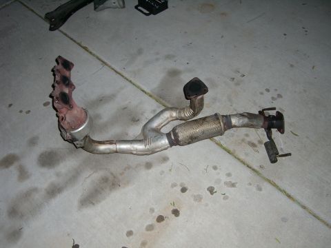 1996 Ford Probe - Automotive exhaust component, including manifold and catalytic converter, lying on a concrete surface.