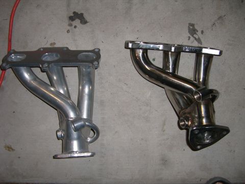1996 Ford Probe - Two exhaust manifolds, one in raw aluminum and the other polished chrome, are displayed on a concrete surface.