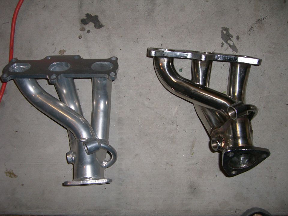 Two exhaust manifolds, one aluminum and one chrome, on a concrete floor