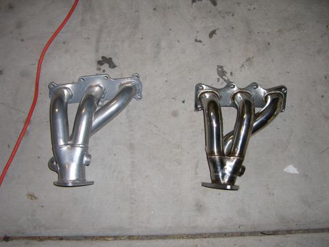 1996 Ford Probe - Comparison of two exhaust manifolds, one with a silver finish and the other with a chrome finish, laid out on a concrete surface.