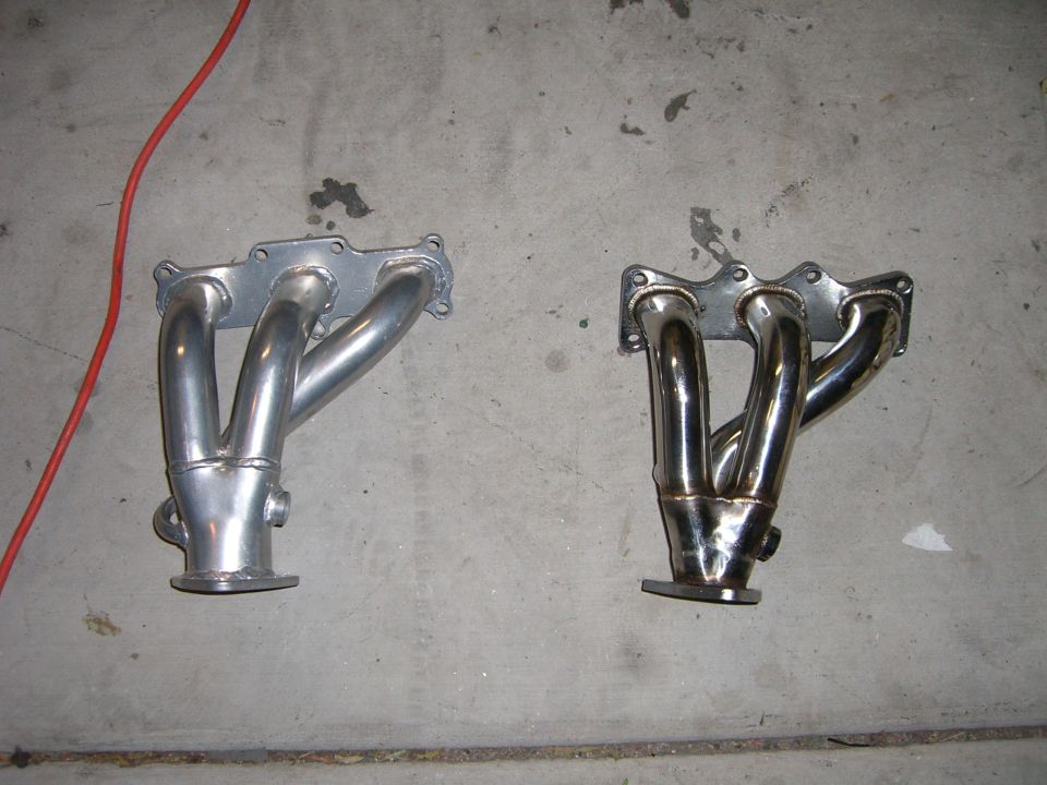 Two exhaust manifolds on a concrete floor, one silver and one chrome