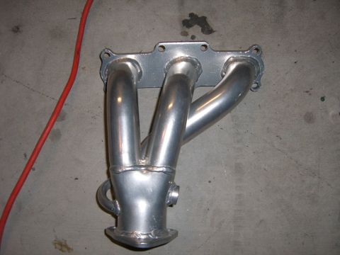 1996 Ford Probe - A silver exhaust manifold sits on a concrete floor next to a red cord.
