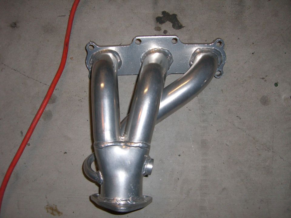 Exhaust manifold with four pipes merging into one collector. It's silver and has a flange at the bottom