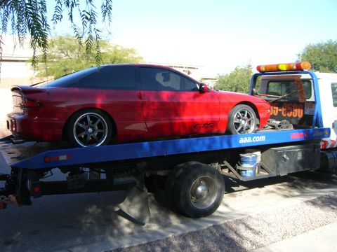1996 Ford Probe - A red coupe is being towed on a flatbed truck. The vehicle has tinted windows and custom wheels.