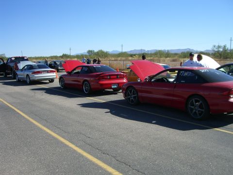 1996 Ford Probe - Several Ford Probes are lined up at a track, with hoods open, under a clear blue sky.