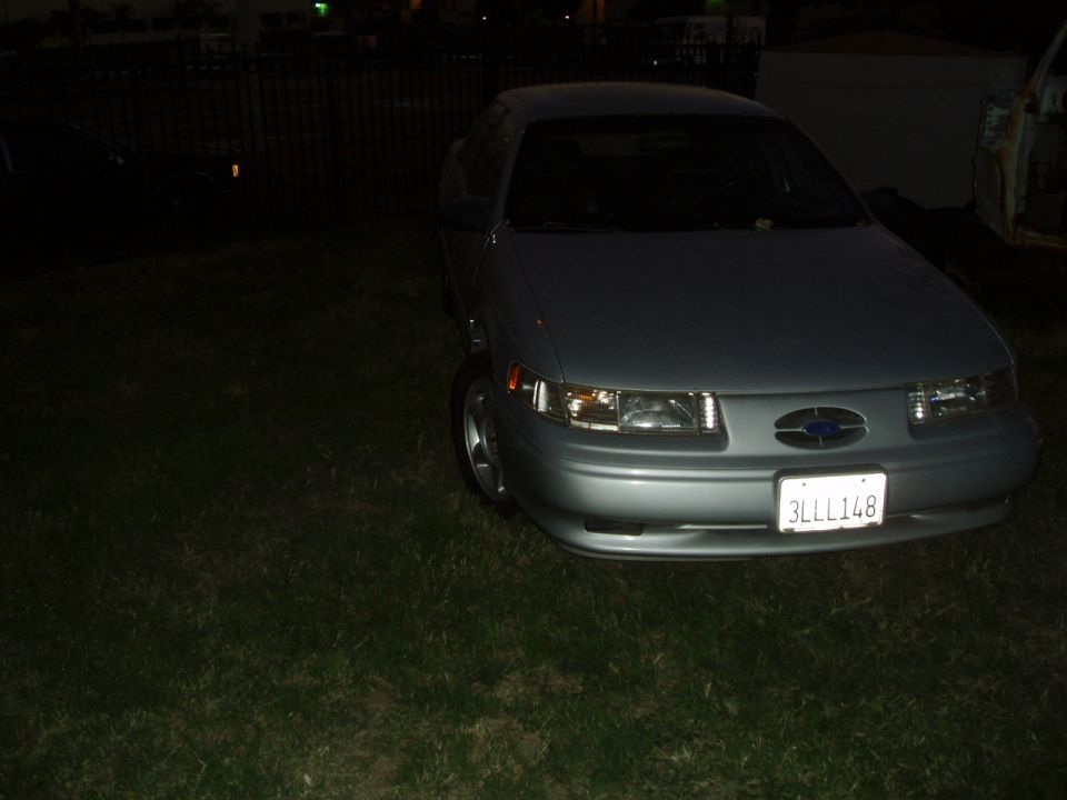 Silver Ford Taurus with a blue oval badge on the grille and license plate 3LLL148