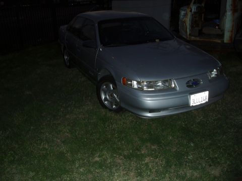 1993 Ford Taurus - A 1993 Ford Taurus is parked on a grassy area at night, with a fence in the background.