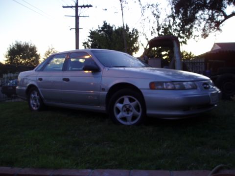 1993 Ford Taurus - A silver sedan is parked on a grassy lawn at dusk, with trees and a structure in the background.