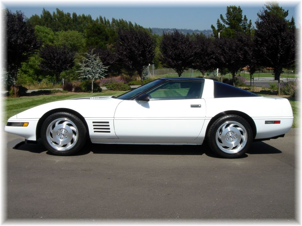 White C4 Chevrolet Corvette coupe with black roof, side view, parked on pavement with trees behind