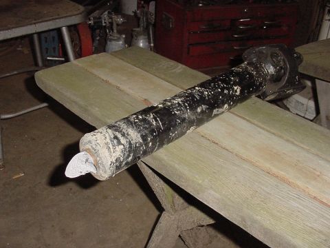 1969 Ford Bronco - A driveshaft, likely from a vehicle, is shown with a protective cap on its end and resting on weathered wooden planks in a workshop setting.