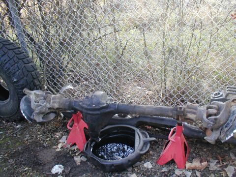 1979 Ford Bronco - Vehicle axle assembly on jack stands, with a drain pan and tire nearby.
