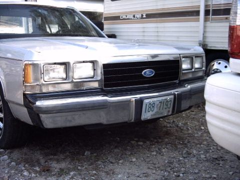 1991 Ford LTD Crown Victoria - The front grille and headlights of a silver Ford Crown Victoria are visible, parked next to a trailer.