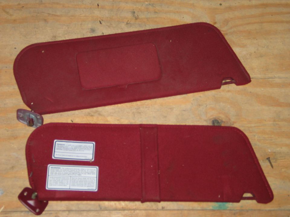 Two red car sun visors with labels on the bottom one, laid on a wooden surface