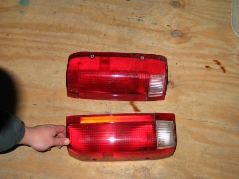 1994 Ford Bronco - Two red taillights are displayed on a wooden surface, with a hand holding the lower one.
