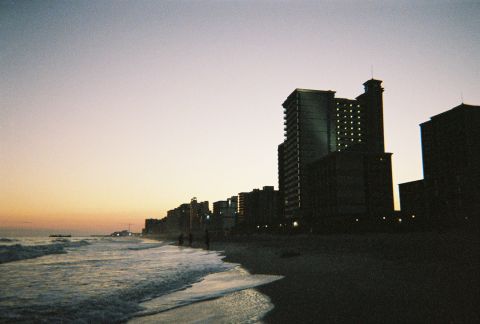 1991 Ford Probe - Ocean waves crash on a beach with a line of buildings in the background during sunset.