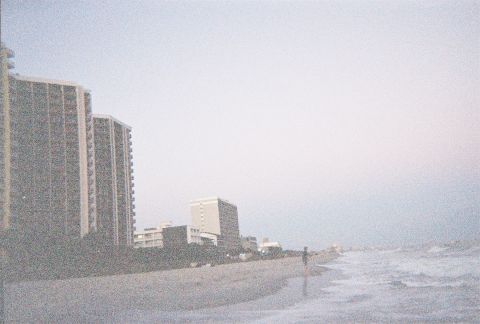 1991 Ford Probe - Coastal scene with buildings and ocean waves on a beach.
