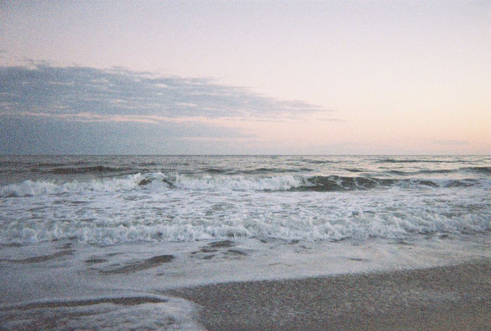 Ocean waves crashing on a sandy beach at dusk with a Supermotors logo in the corner