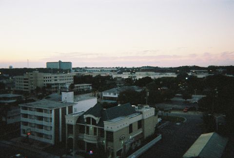 1991 Ford Probe - A wide view of a city at dusk, various buildings and trees, with the Supermotors logo in the lower right corner.