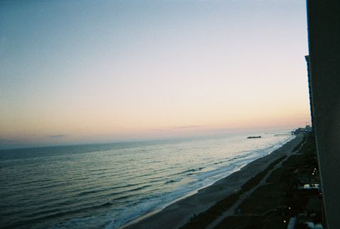 1991 Ford Probe - Sunset over the ocean and beach, with a pier and buildings in the distance.