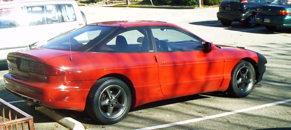 Red Ford Probe coupe parked in a lot, rear three-quarter view with gray five-spoke alloy wheels