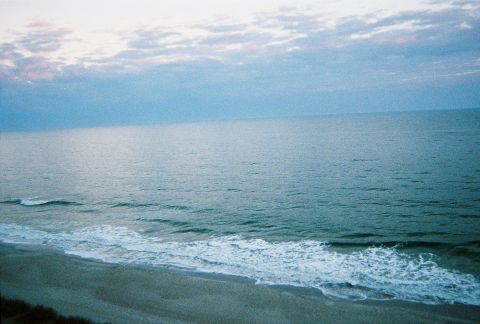 1991 Ford Probe - A ocean scene with waves rolling onto the shore, under a sky filled with soft clouds. The Supermotors.net logo is present in the corner.