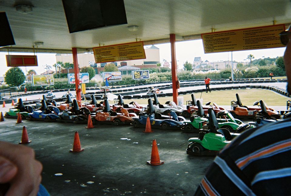 Go-karts lined up under a covered area at a track. Orange cones are on the ground