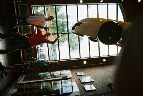 1991 Ford Probe - A white car is suspended from the ceiling in a museum-like setting, with people posing below.