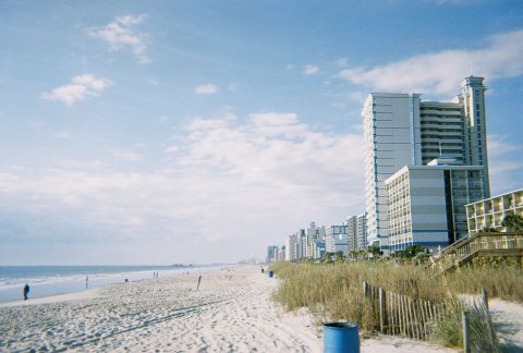 1991 Ford Probe - A view of a beach with hotels lining the coast under a partly cloudy sky.