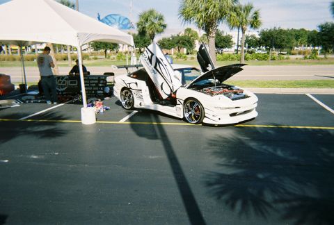 1991 Ford Probe - A customized white sports car is displayed with its doors and hood open, revealing its engine and interior modifications.