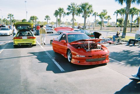 1991 Ford Probe - A red sports car is parked with its hood open, alongside other vehicles at an outdoor event.