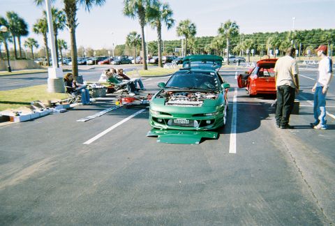 1991 Ford Probe - Two cars are parked in a lot, one with its hood open, while people sit nearby.