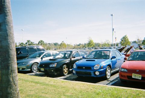1991 Ford Probe - A blue Subaru WRX is parked in a lot alongside other vehicles under a clear sky.