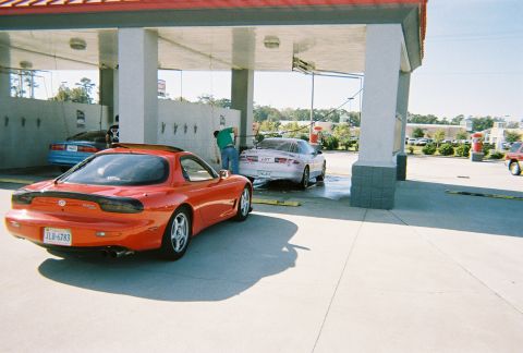 1991 Ford Probe - A red Mazda RX-7 is parked at a car wash, with another vehicle being washed in the background.
