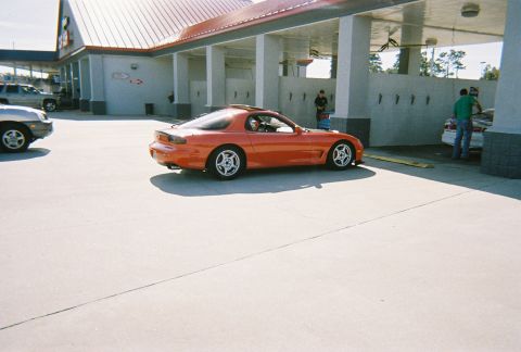 1991 Ford Probe - An orange Mazda RX-7 is parked outside a car wash with another vehicle being attended to.