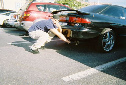 1991 Ford Probe - Man inspects the exhaust on a black 1991 Ford Probe in a parking lot.