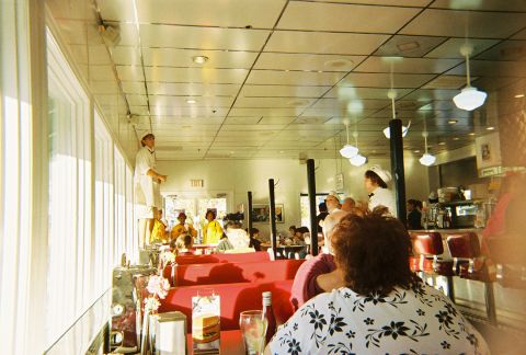 1991 Ford Probe - Interior view of a diner with patrons and staff, red booths and a counter area.