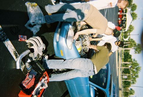 1991 Ford Probe - A group of people are actively working on the engine of a blue car, with another vehicle in the background.