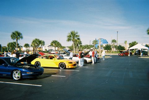 1991 Ford Probe - Several cars are parked in a lot under a clear blue sky, with some people gathered around.