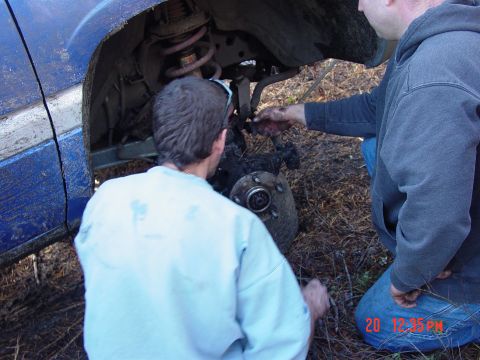 1995 Dodge 1500 - Two people are working on the exposed suspension and wheel hub of a blue vehicle in an outdoor setting.
