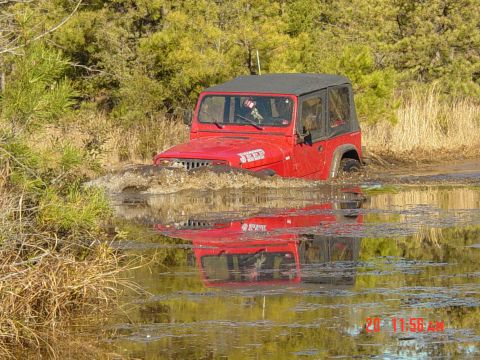 1995 Dodge 1500 - Red Jeep Wrangler navigating through a water obstacle, its reflection mirrored in the water.