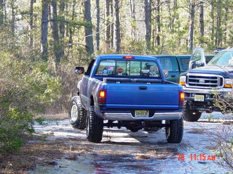 1995 Dodge 1500 - Blue pickup truck navigates a muddy, wooded trail with another vehicle following behind.