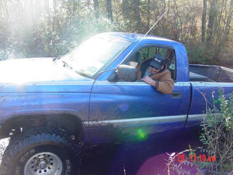 1995 Dodge 1500 - A blue pickup truck is stuck in the mud with a person wearing a police hat inside.